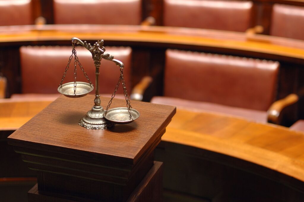 Scales of justice on a wooden podium, set against an empty courtroom with brown leather seating, symbolizing law and fairness.