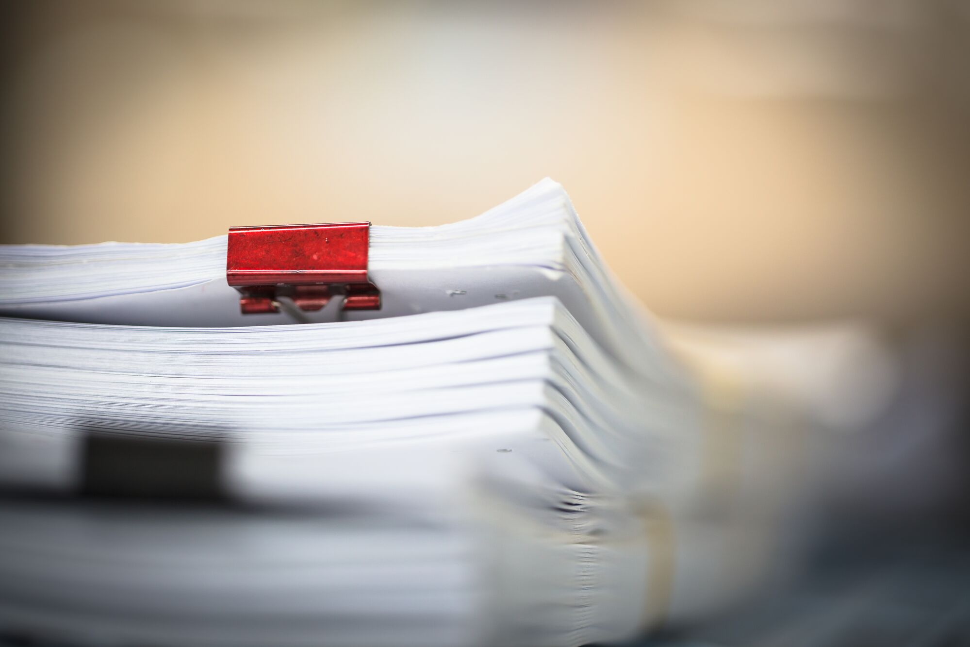 A stack of paper secured with a red binder clip, emphasizing organization and document management, relevant for office or administrative contexts.
