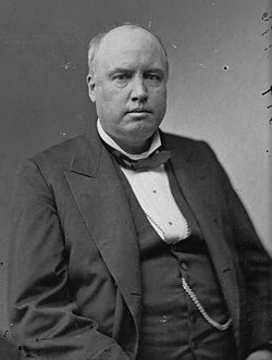 Portrait of a man in formal attire, featuring a dark suit and bow tie. He appears serious, suggesting a dignified or professional context.