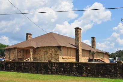 Abandoned building with stone walls and four chimneys, set against a cloudy sky. The property is fenced, suggesting prior use or significance.