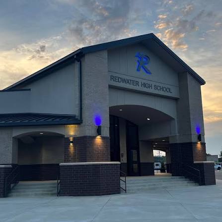 Redwater High School entrance featuring the school name illuminated above the doorway, accompanied by blue accent lights and a sunset backdrop.