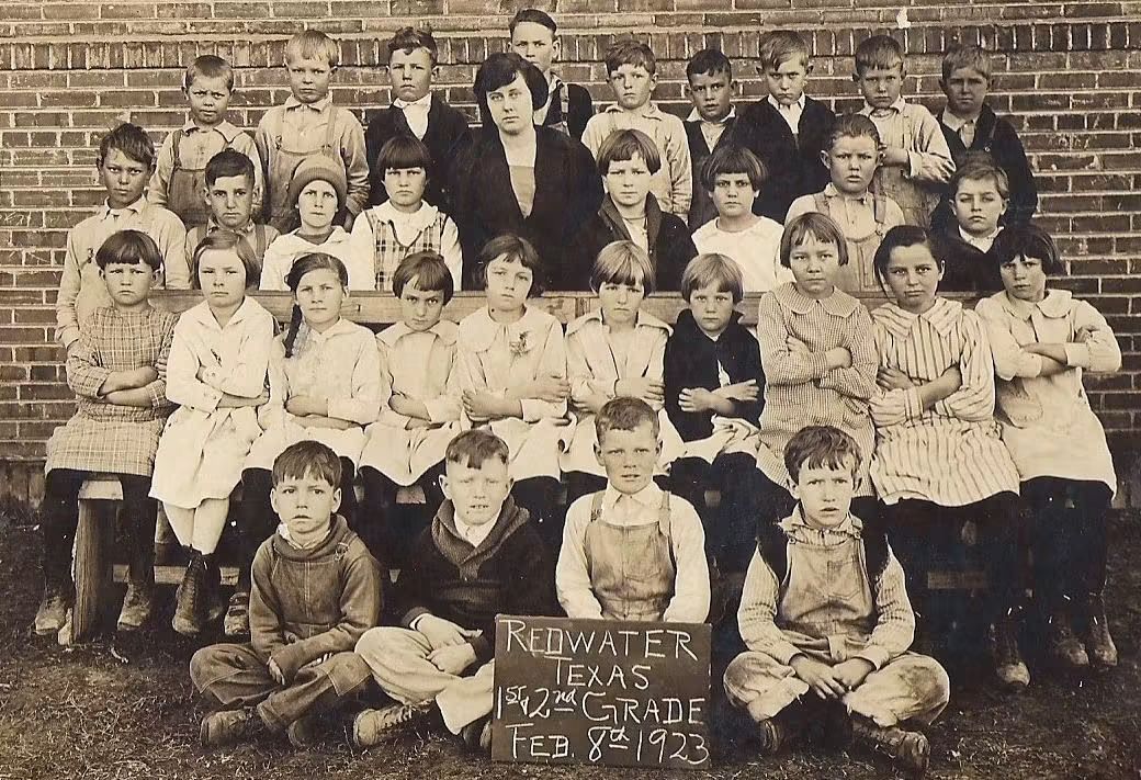 Black-and-white photo of a 1923 first and second-grade class in Redwater, Texas, featuring students seated with an academic sign.